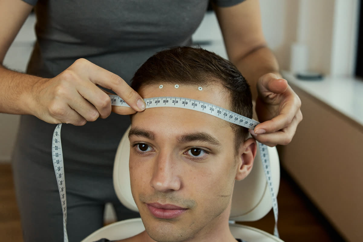 A practitioner holds a soft tape measure across the top of a seated man's head to mark sensor positions before a session.